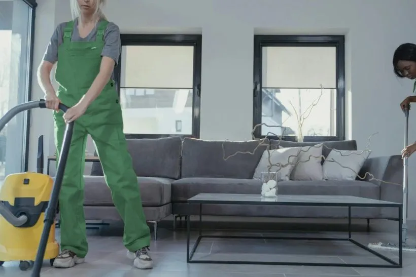Cleaner vacuuming the floor of a bright living room