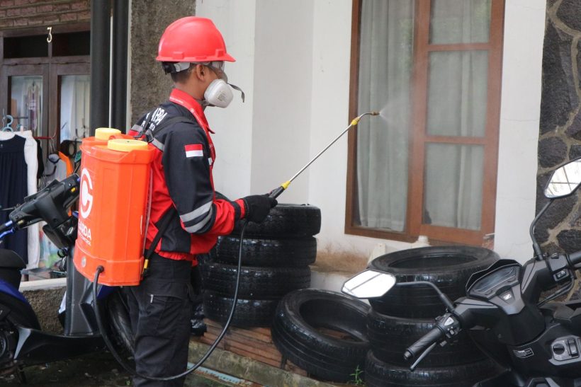 Pest control worker in safety gear spraying treatment around a building